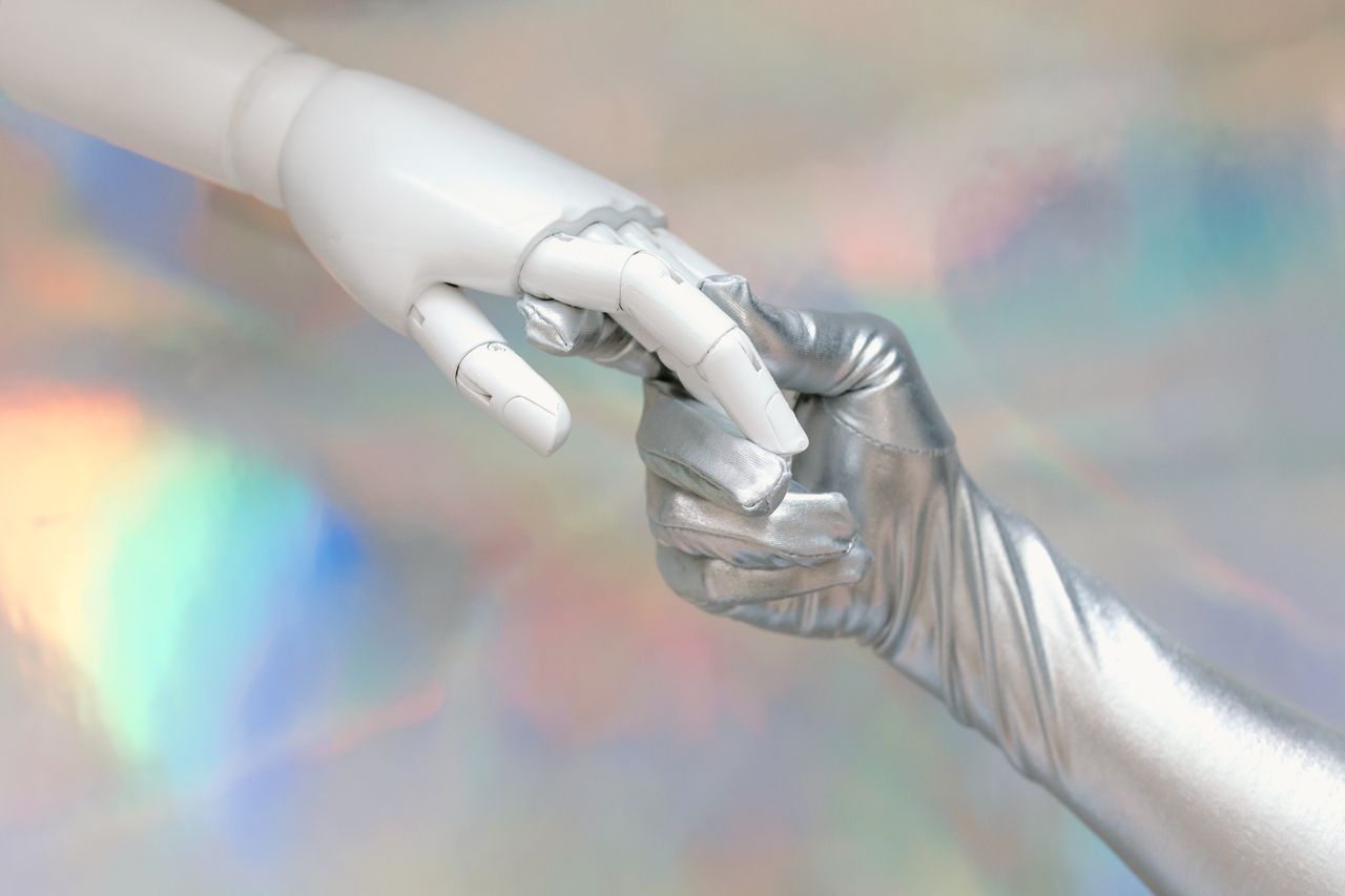 wedding-photography-02 Close-up of a robot hand and silver-gloved hand touching, symbolizing human-robot connection.